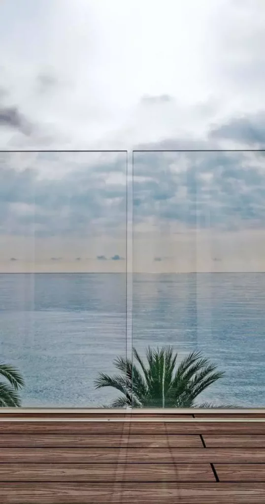 Parapetto in vetro trasparente Garda AP su balcone con pavimento in legno e vista sul mare calmo sotto un cielo nuvoloso.