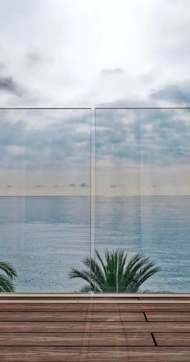 Parapetto in vetro trasparente Garda AP su balcone con pavimento in legno e vista sul mare calmo sotto un cielo nuvoloso.