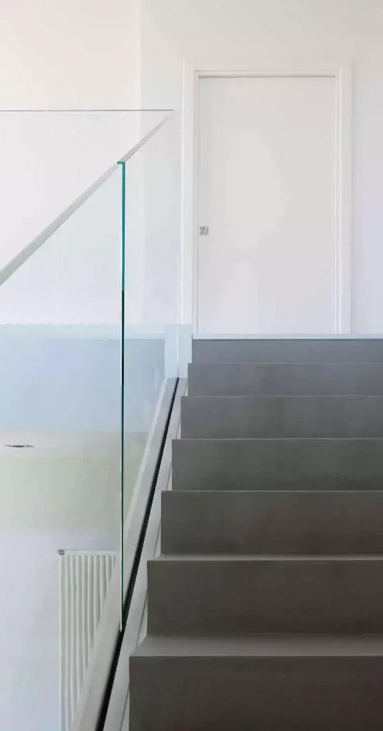 Scala moderna con gradini grigio scuro e balaustra Garda FS in vetro extra-chiaro che conduce a una porta bianca.
