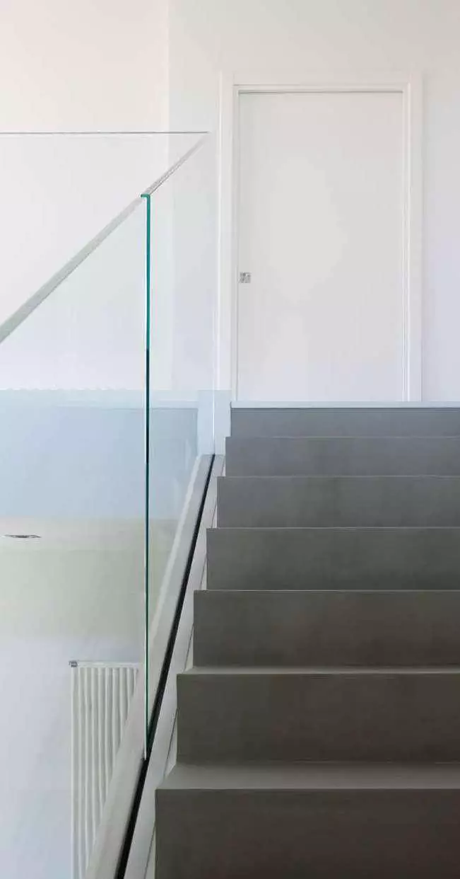 Scala moderna con gradini grigio scuro e balaustra Garda FS in vetro extra-chiaro che conduce a una porta bianca.