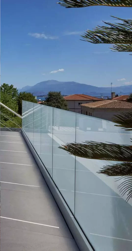 Terrazza esterna con pavimentazione grigia e lunga balaustra in vetro basata su modello Garda SP inclinata con vista panoramica su montagne e tetti.