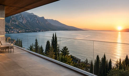 Ampia terrazza moderna con parapetto in vetro trasparente e vista panoramica su un lago e montagne al tramonto.